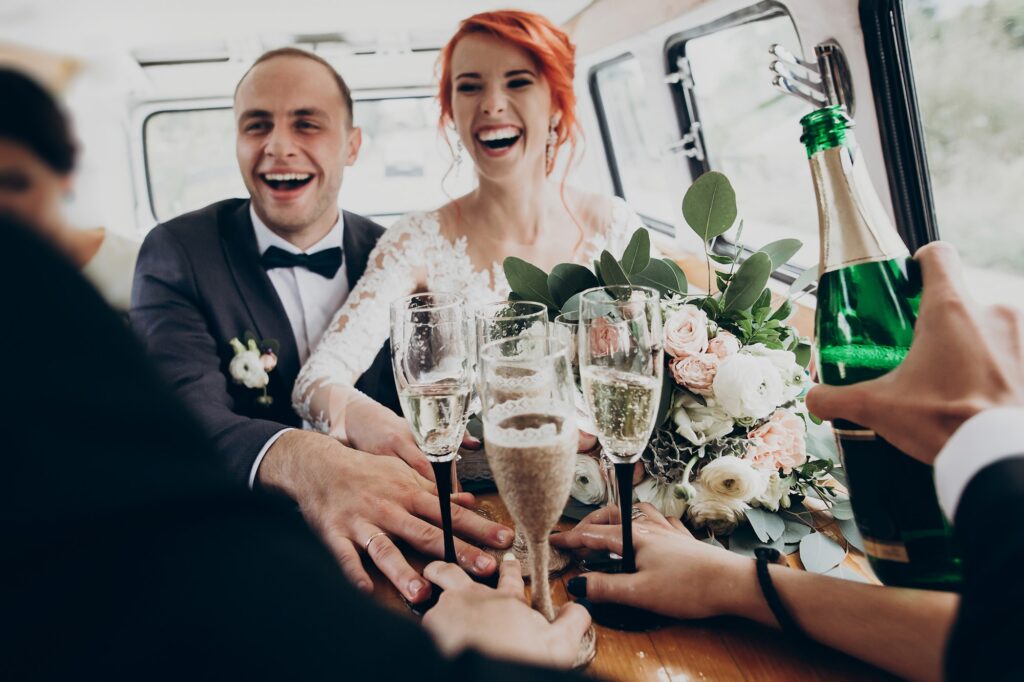 Stylish happy bride and groom toasting with glasses of champagne and having fun